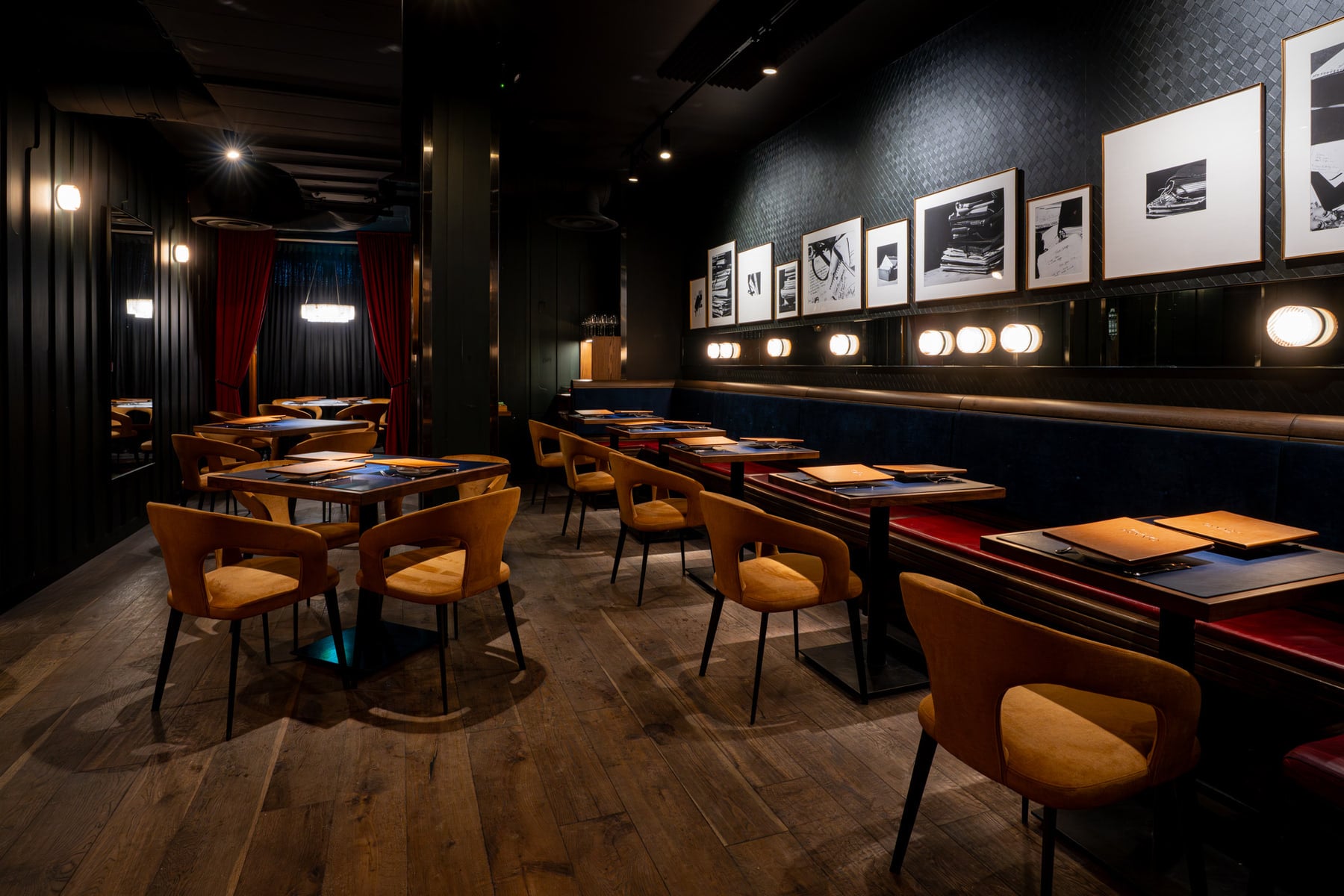 Pasta Privato's dining room in Toronto — dark panelled walls hung with framed black-and-white prints, mustard-velvet chairs, deep navy banquette, burgundy curtains beyond, wood plank floor