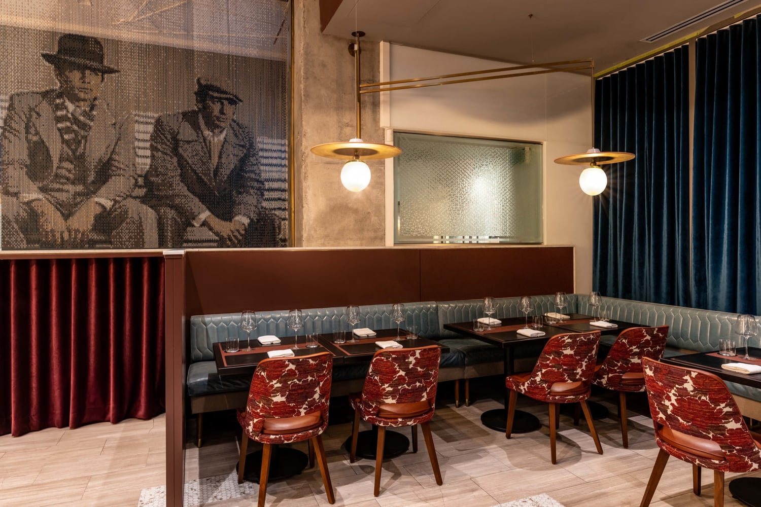 Restaurant Lucie's dining room in Toronto — burgundy velvet curtains, blue banquettes, monochrome portrait diptych on a textured wall, brass pendants overhead
