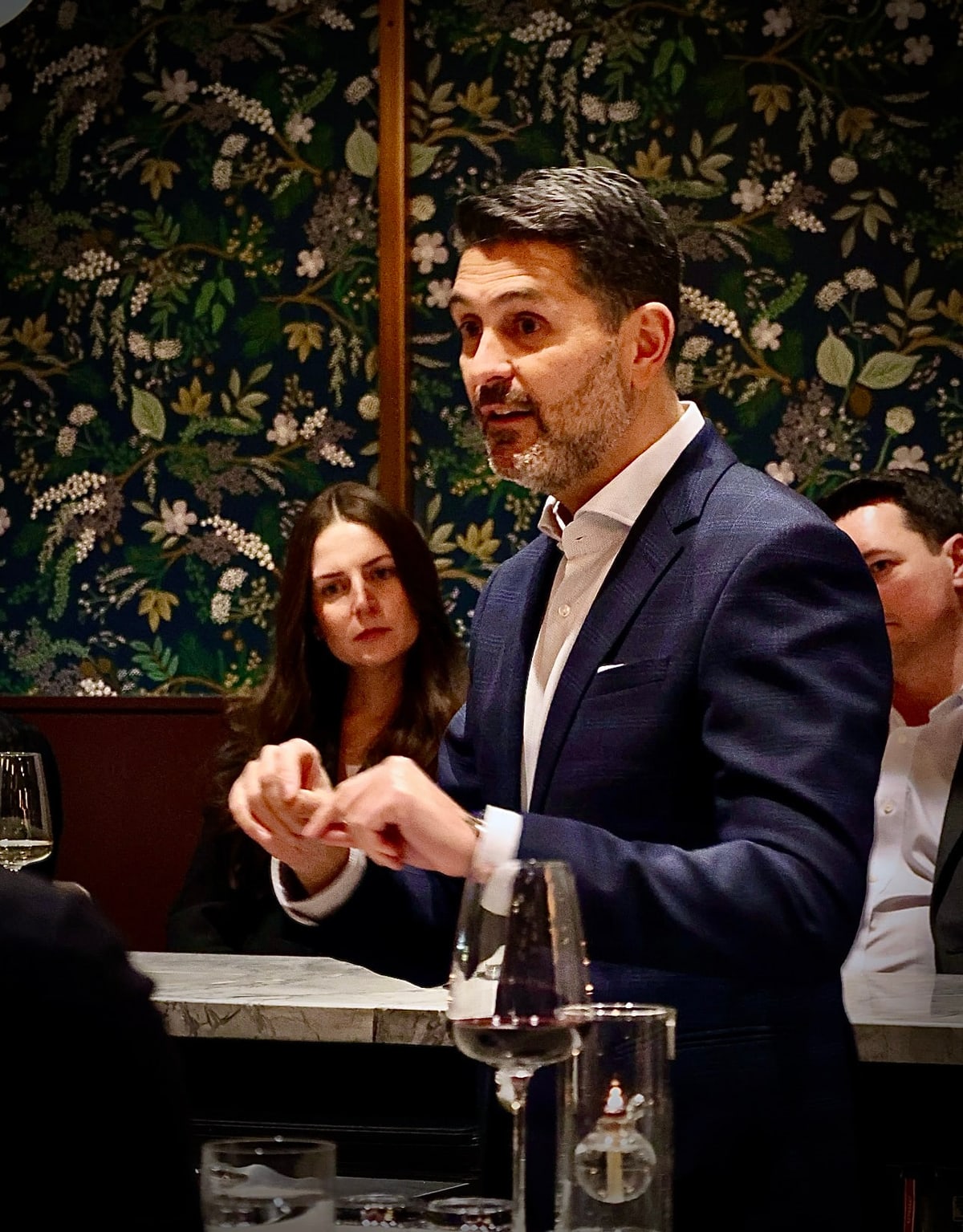 Yannick Bigourdan speaking at a private dinner with floral wallpaper, a guest at the table thinking through the point — a standard getting named out loud